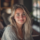 Femme souriante aux cheveux blonds, intérieur lumineux.